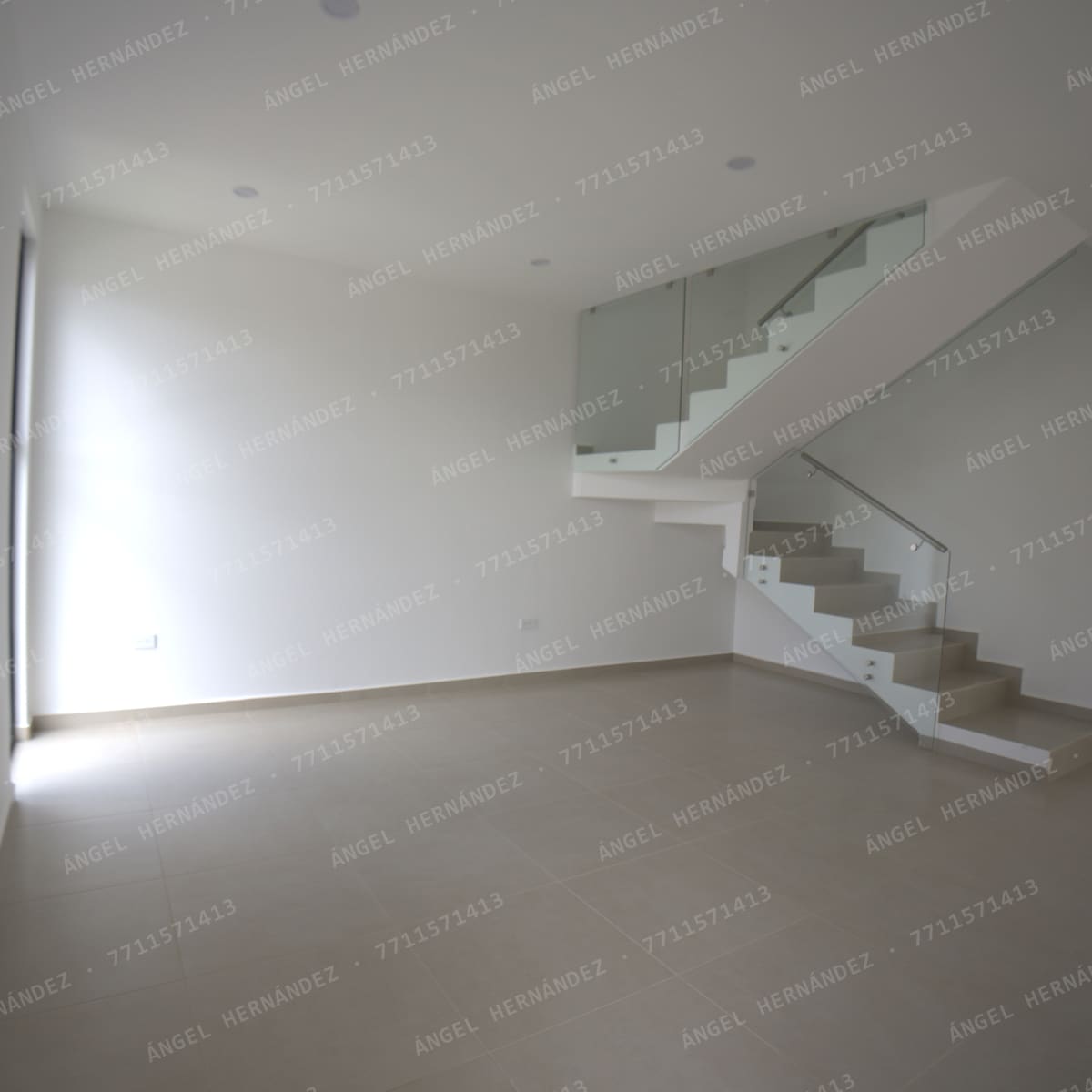 Sala de planta baja con escalera de barandal de vidrio en Fraccionamiento Los Olivos